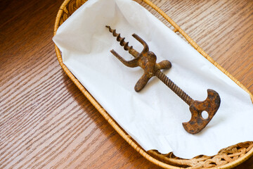 Vintage old rusty wine corkscrew. Corkscrew on a white napkin on a wooden wicker plate. Winemaking. Wine opener.