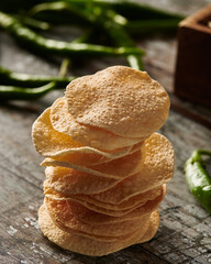 Mini Poppadum stack closeup on a wooden table with fresh green chili and backlighting