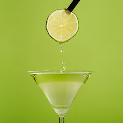 Slice of lime dripping into martini glass graphic plain green background isolated