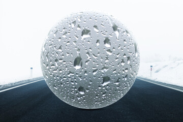 Big glass orb with rain droplets surface. Concept frozen icy and wet winter asphalt road.