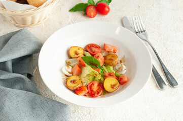 Rustic salad with baked potatoes, vegetables and quail egg. Dressed with mustard sauce. On a white plate. Nearby is a fork with a knife and a napkin.