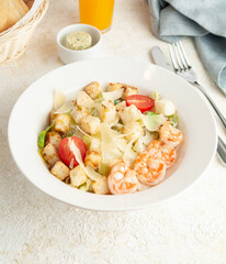 Caesar salad with shrimps. On a white plate. Nearby are cutlery and a blue napkin. Light background top view.