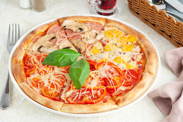 Pizza with four different fillings. Decorated with basil. On a white plate. Nearby is a fork, spices and a glass of juice. Light background close-up.