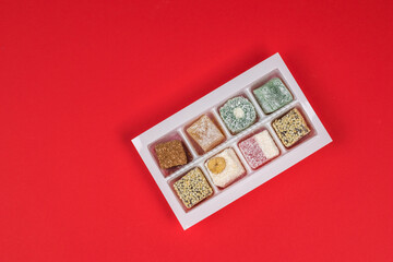Turkish delight in a plastic container on a red background. Flat lay.