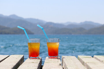 Two glasses with cocktail on a wooden pier on sea and mountains background. Summer vacation on a...