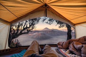 Traveler man relaxing and taking the view of Bromo active volcano inside a tent in the morning