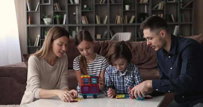 Family play with little children magnetic construction set making creative vehicle, spend weekend together at modern cozy living room, having fun chatting enjoy playtime at home. Leisure games concept