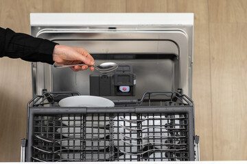 Woman placing spoon inside of dishwashers upper drawer