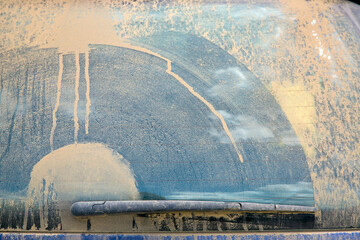 dirty heated rear window covered with a layer of dust with a wiper blade swipe close-up, dirty blue car. - obrazy, fototapety, plakaty