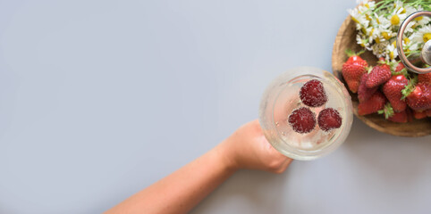 
Top view of female hand holding alcohol drink or cocktail and strawberries isolated on bright gray...