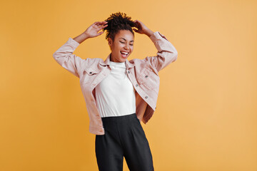 Inspired black girl in jacket posing with hands up. Studio shot of relaxed african american woman isolated on yellow background.