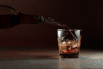 Whiskey is poured from a bottle into a frozen glass with natural ice.