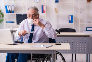 Fototapeta premium Old male employee in wheel-chair drinking coffee during break