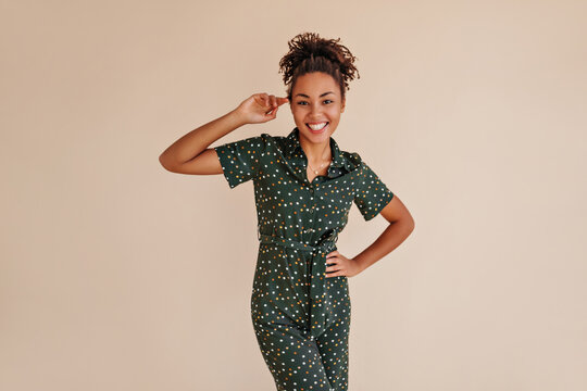 Romantic black girl posing with hand on hip. Studio shot of glamorous african american woman in green overalls.
