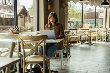 Stylish teleworker using laptop near menu in cafe.