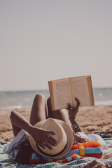 Vertical camera position of a black girl lying on the beach holding a book while looking forward on...