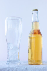 An empty beer glass with ice stands on a white background next to a full bottle of beer
