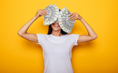 Young happy excited beautiful woman emotionally looking in the camera with a lot of money in her hands and having fun isolated on yellow background © My Ocean studio