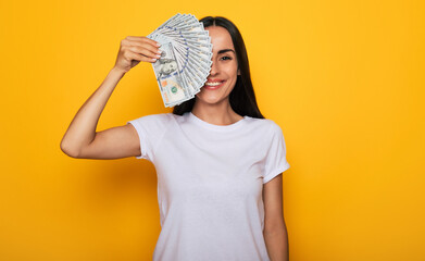 Young happy excited beautiful woman emotionally looking in the camera with a lot of money in her hands and having fun isolated on yellow background