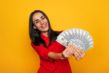 Young happy excited beautiful woman emotionally looking in the camera with a lot of money in her hands and having fun isolated on yellow background