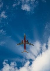 A passenger plane from below against the blue sky and sun rays coming out of clouds. The aircraft...