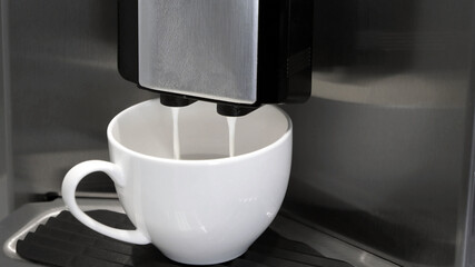 Fully automatic Espresso Maker coffee machine pouring milk in coffee cup.