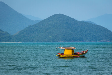 Fototapeta na wymiar Small wooden boat sails in the clear waters of Ubatuba Bay
