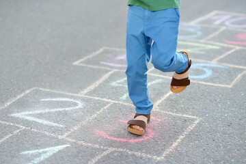 Naklejka na ściany i meble Little boy's legs and hopscotch drawn on asphalt. Child playing hopscotch game on playground on spring day.