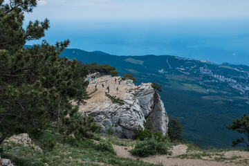 Crimean pines, curved by the wind, on a sunny rock. In the distance mountains covered with forests, blue sky, clouds., Botkin Trail, Stavri-Kaya rock Yalta, Crimea.