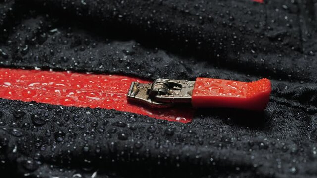 Water droplets on the waterproof fabric. Close-up of a waterproof jacket. Black clothes with red zipper