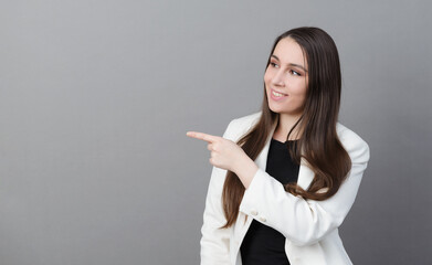 1 young woman with long hair in a white jacket  smiles , points to the side on a gray