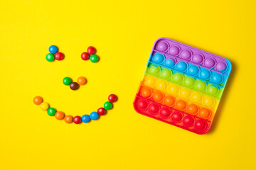 Rainbow silicone sensory antistress pop it toy with smiley from colorful candies on yellow background.