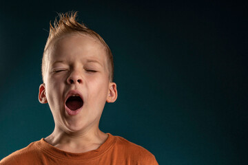 portrait of a boy with blond hair yawns. the child wants to sleep. kid boy yawns