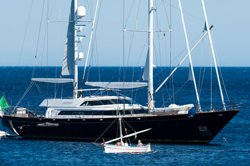 Fototapeta premium Stunning view of an old, wooden boat with tourists on board sailing in front of a luxury yacht.Sardinia, Italy. Concept of difference between rich and poor.
