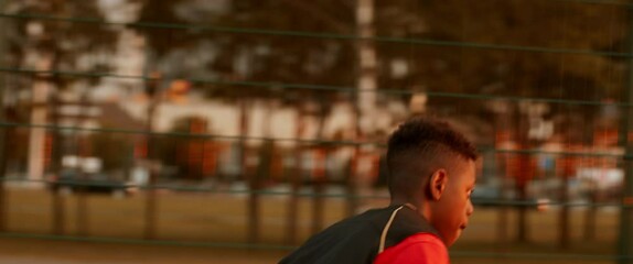 Black African American teenager kid boy playing basketball alone on an outdoor court in the evening. High quality 4k footage