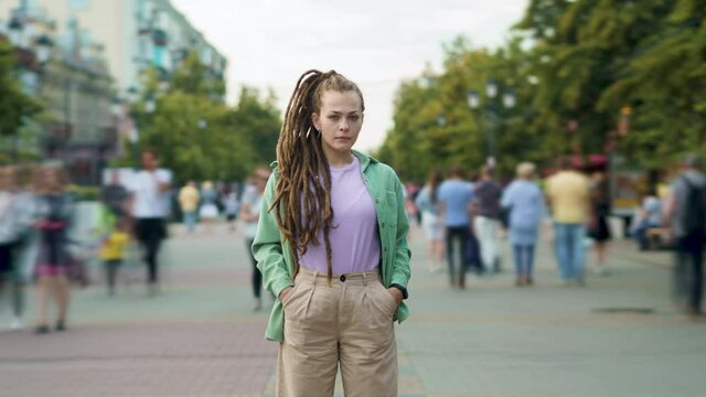 Time lapse of confident young woman with dreads standing outdoors alone in urban street and looking at camera against city background. People and public places concept.