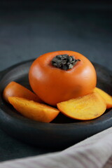 ripe orange persimmon fruit in a wooden dish.Persimmon fruit on a dark background, persimmon fruit. dietary seasonal product