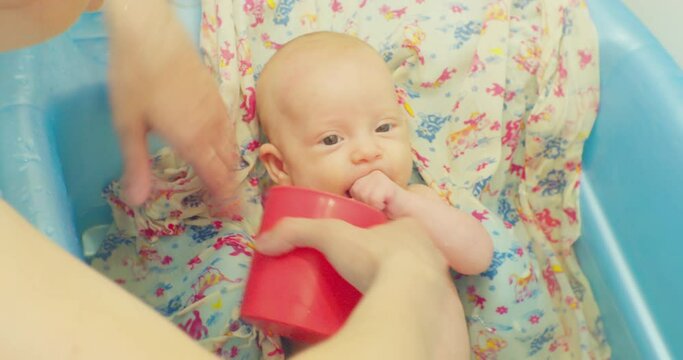 female hands wash a little cute baby lying on a bright sheet in a baby bath.