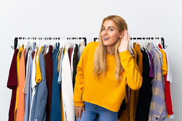 Young Uruguayan blonde woman in a clothing store listening to something by putting hand on the ear