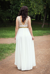 Brunette stands in a white long dress with a deep cut on her back