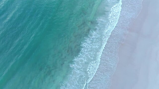 Aerial footage of the tuquoise waters of the Atlantic Ocean with surf rolling in on deserted Daytona Beach, Florida taken at dawn.