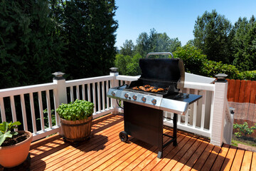 Close up of an BBQ cooker with lid open displaying smoke coming out while on home outdoor wooden deck - 443493929