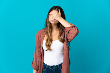 Young caucasian woman isolated on blue background covering eyes by hands. Do not want to see...