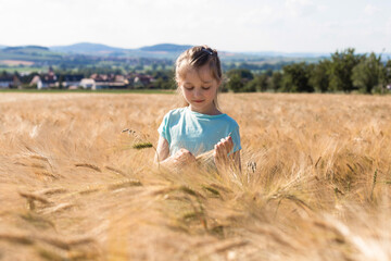 The concept of freedom and unity with nature. Summer vacation. Relaxation. A cute charming girl with long hair stands in a field of spikelets.