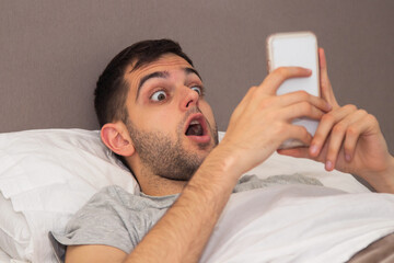 man in bed looking at mobile phone surprised or scared