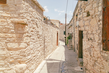 Sunny narrow street in old village Omodos on Cyprus. Stone walls and vibrant green plants on a sunny day.