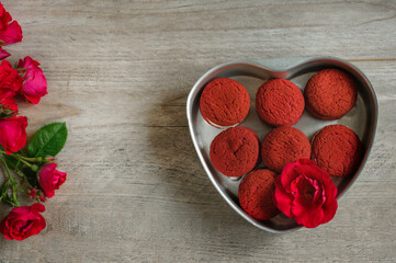 Heart-shaped red cookies in a metal bowl. Gray wooden background roses and sweets. Copy space for text. Top view