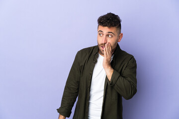 Caucasian man isolated on purple background whispering something with surprise gesture while looking to the side