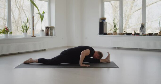 Professional trainer practices flow yoga in private class. Adult man makes yoga asanas on a mat in white bright studio. Fitness, healthy lifestyle and wellness concept.