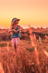 A little girl walks across the field at sunset. Summer vacations and rest in the village.